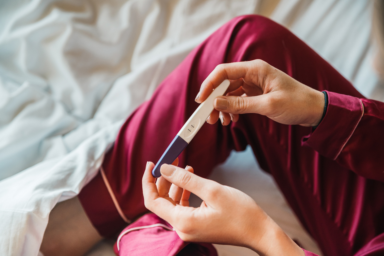 woman in bed looking at pregnancy test