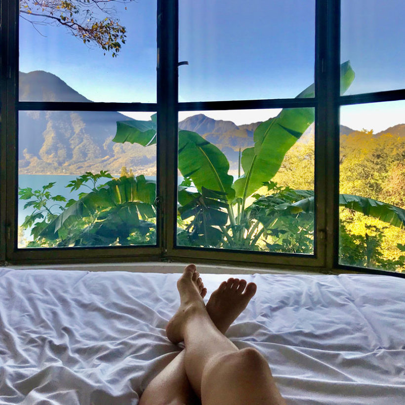 shot of woman's legs laying on bed with window overlooking a mountain