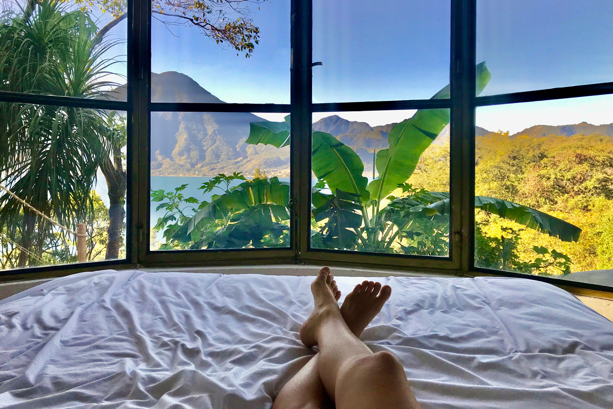 shot of woman's legs laying on bed with window overlooking a mountain