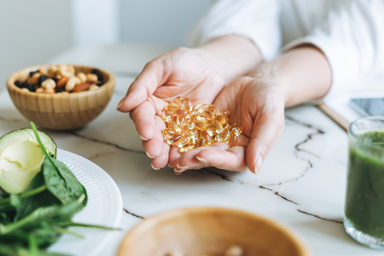 Woman Hands In White With Omega 3, Vitamin D Capsules With Green Vegan Food