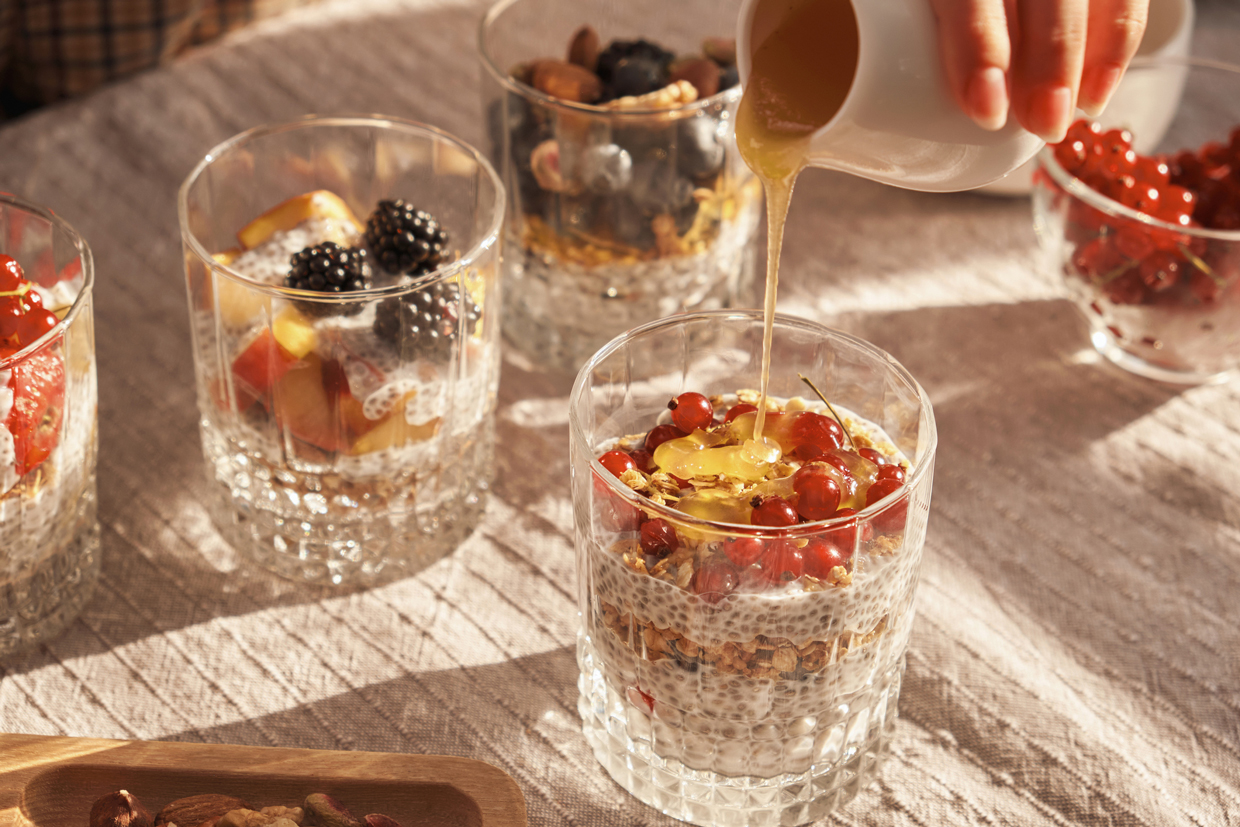 honey over a ready-made vegetarian chia pudding dessert with soy milk, fresh berries and pieces of ripe fruit, decorated with nuts and muesli