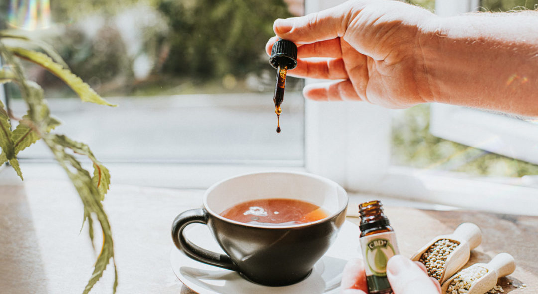Hand holding CBD dropper over tea