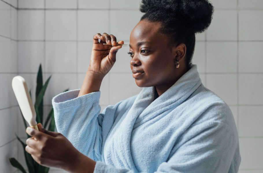 woman plucking eyebrows with tweezers in bathroom
