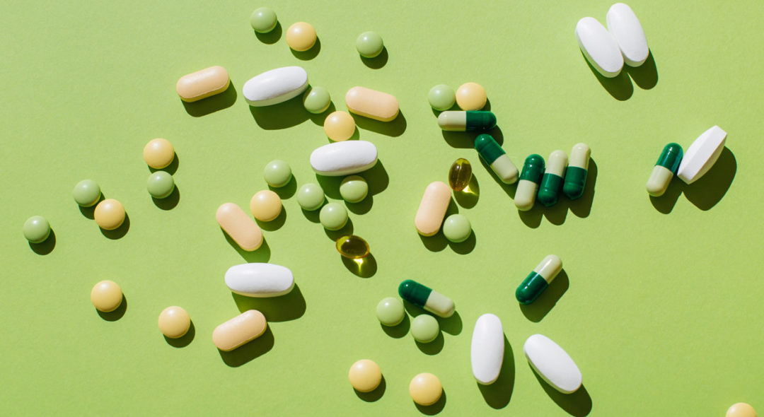 Colorful pills and capsules on green background