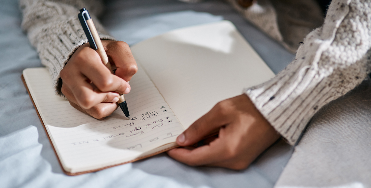 Cropped shot of a man writing in a notebook on his bed at home