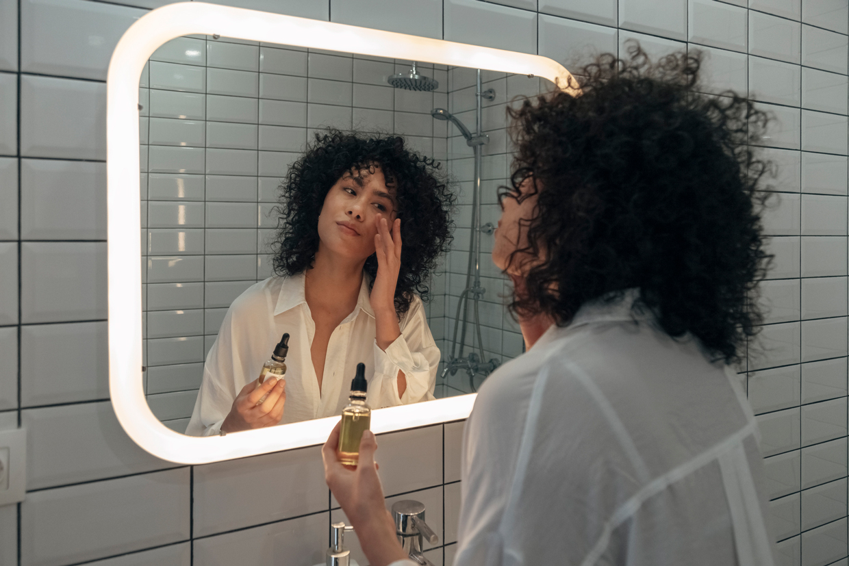 woman gently applying face oil serum with fingers in modern bathroom.