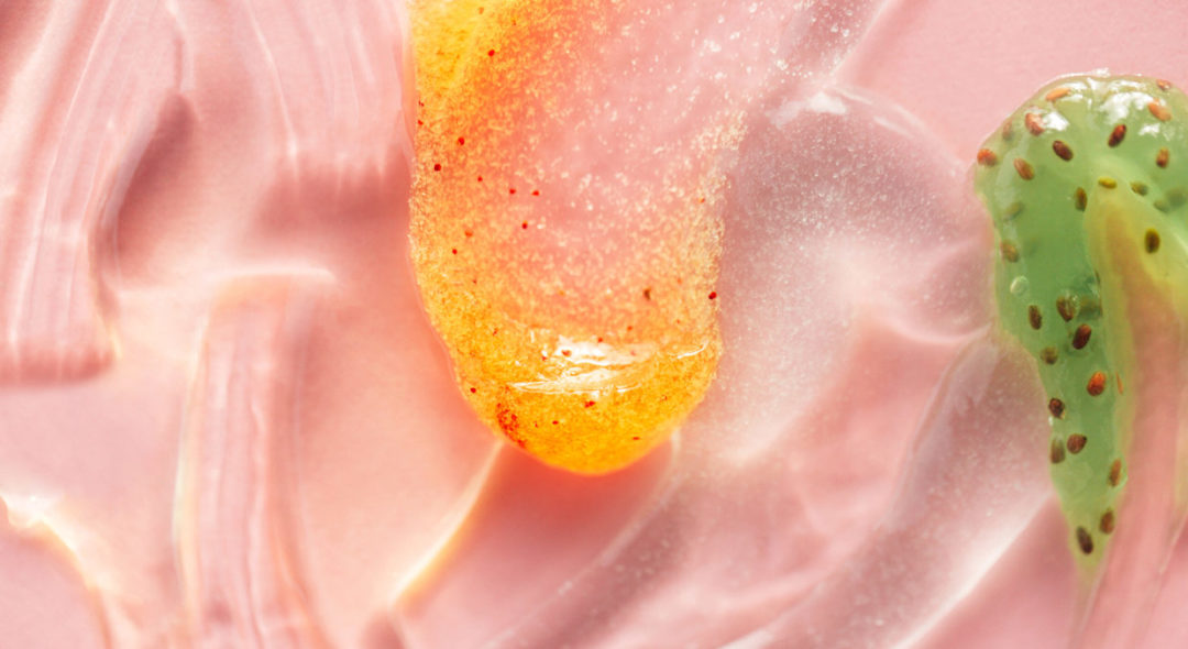 Textured smear of orange and kiwi jelly with seeds on pastel pink background