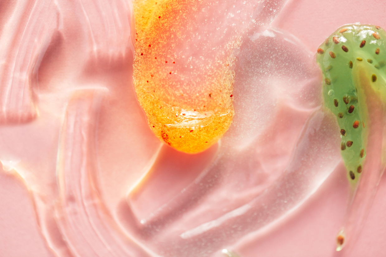 Textured smear of orange and kiwi jelly with seeds on pastel pink background