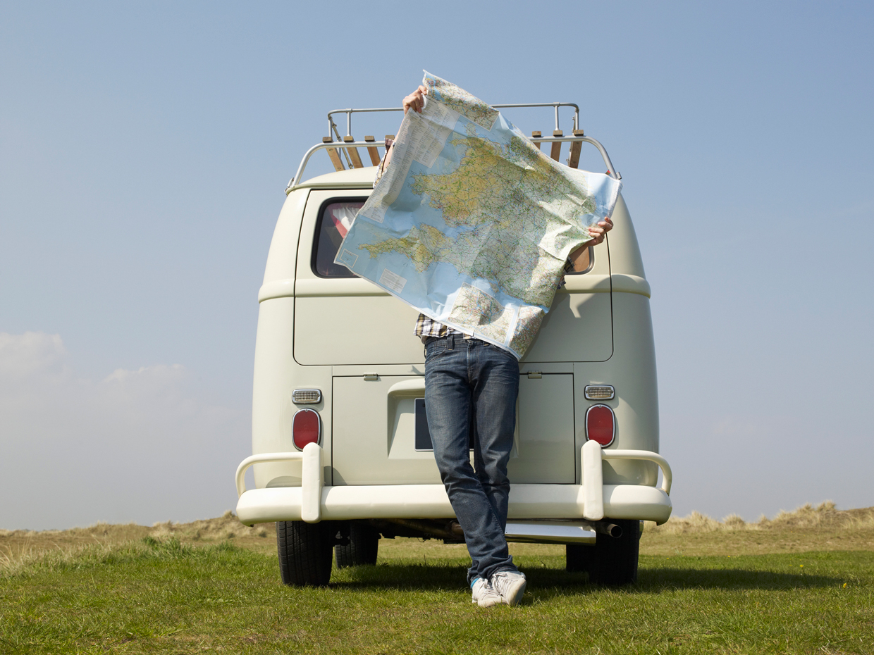 Young Male holding up map on a windy day whilst leaning against camper van