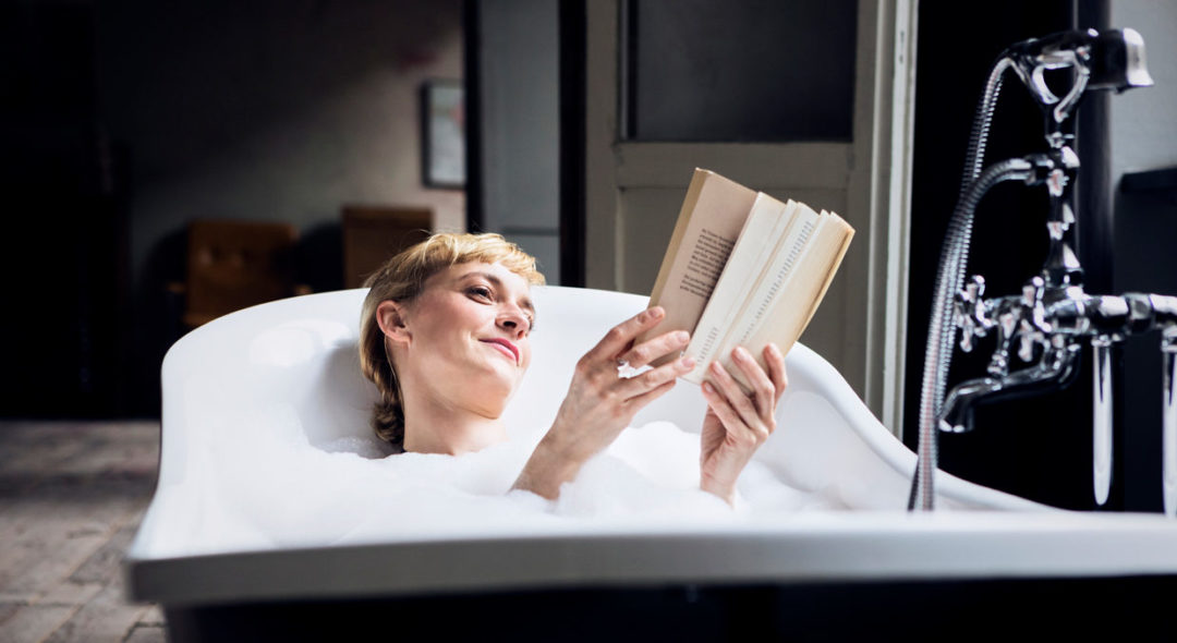 woman taking bubble bath in a loft reading a book