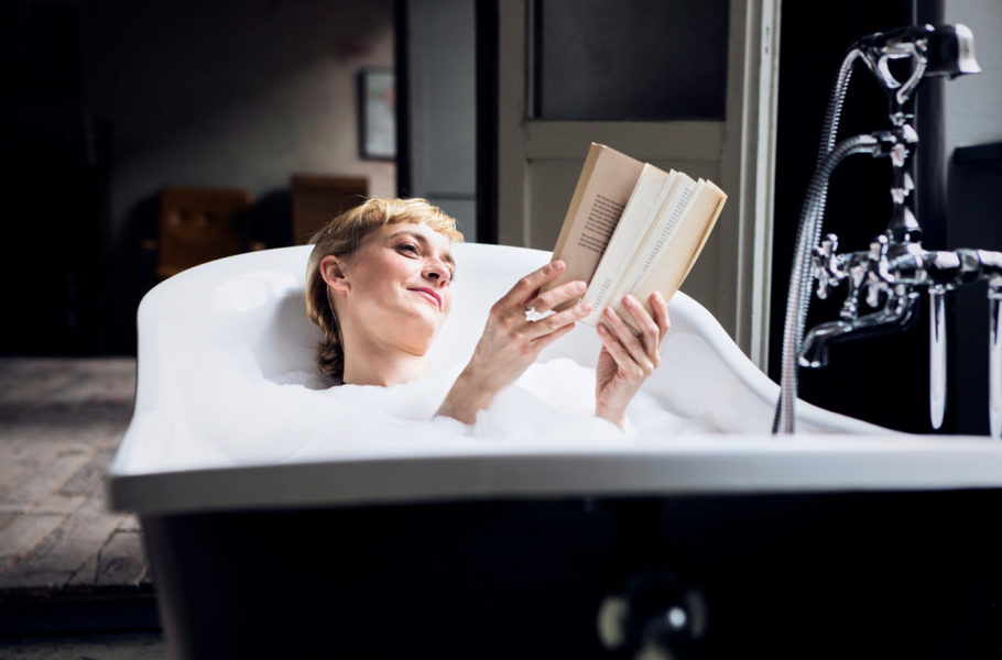woman taking bubble bath in a loft reading a book