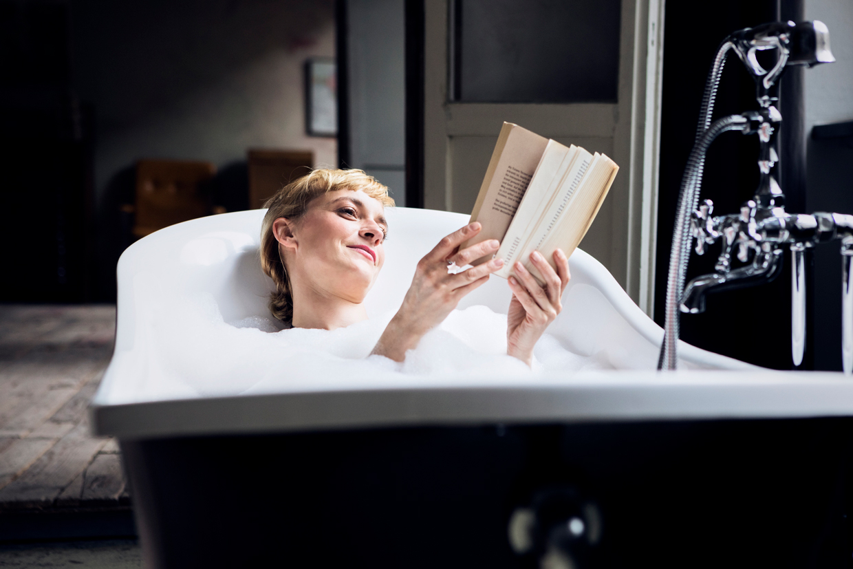 woman taking bubble bath in a loft reading a book