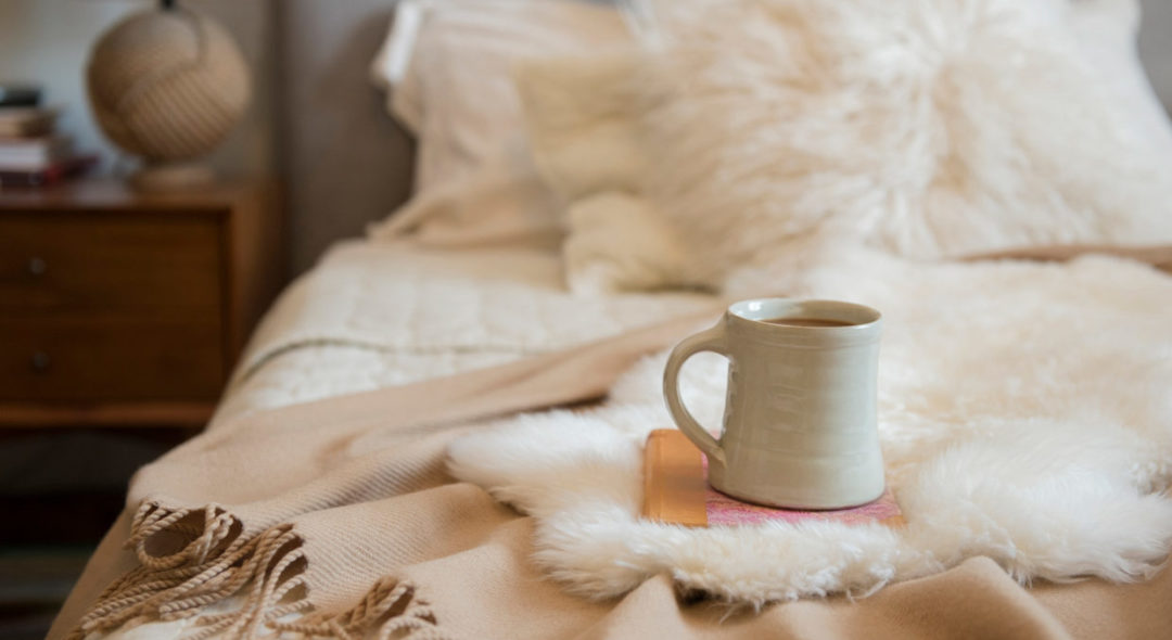 Coffee cup and book on fur on bed