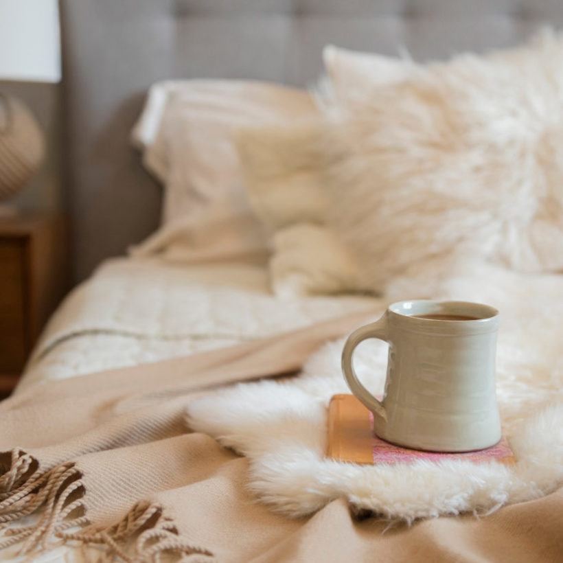 Coffee cup and book on fur on bed