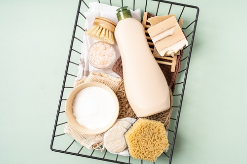 Eco friendly natural cleaners. Basket with baking soda, dish brush, soap, sponge on green background. Organic ingredients for homemade cleaning with mockup bottle