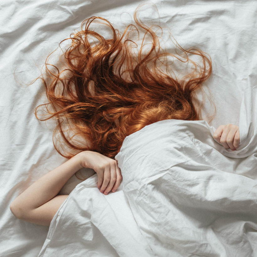 woman pulling bed covers on her face