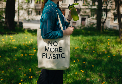 Woman holding reusable cotton zero waste bag with text No More Plastic