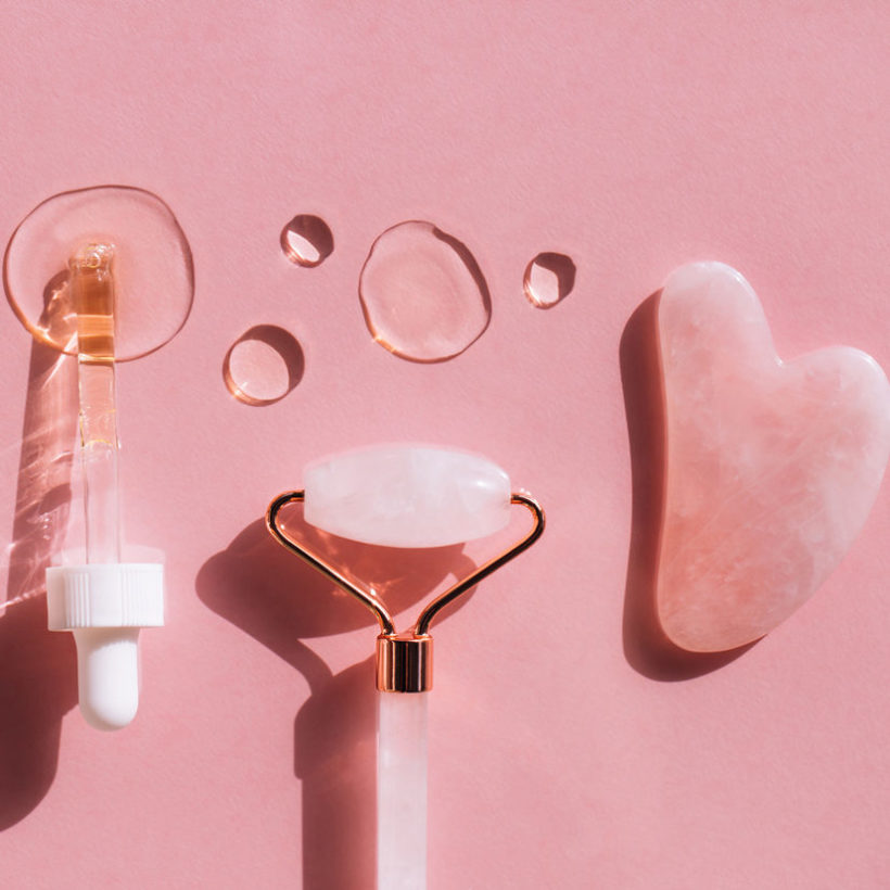 Quartz massager guasha, quartz face roller, pipette and hyaluronan acid drops on pink background