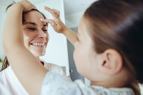 Daughter putting facial cream on mother’s face -