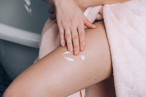 Woman applies moisturizing lotion to her thigh