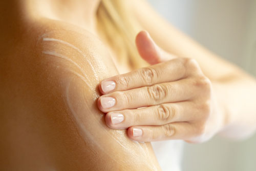 woman applies a moisturizing lotion on her shoulder