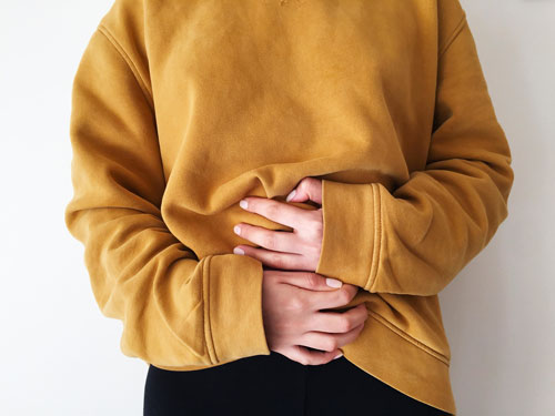 woman in yellow sweater holding stomach