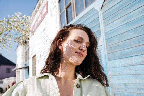 woman standing at the blue wooden wall with floral shadows on her face