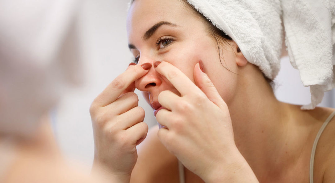 Reflection of woman with towel on head squeezing blackhead on her nose side
