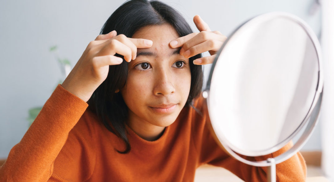 woman Squeezing acne skin and looking on the mirror at home