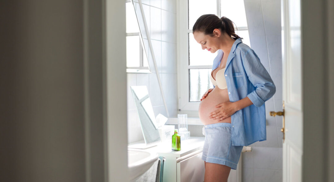 pregnant woman holding belly in bathroom