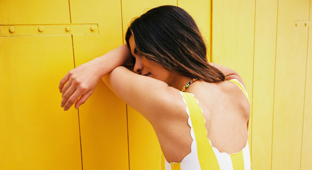 woman in yellow swimsuit leaning on yellow wall