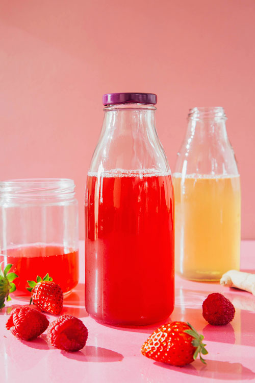 bottle of fruit drinks with strawberries on pink background