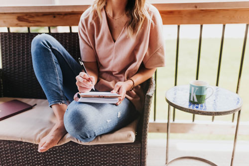 Woman writes in notebook outside on her porch