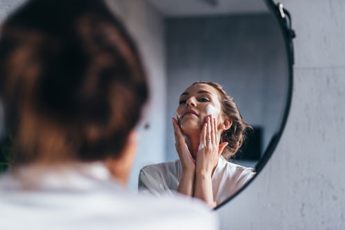 Woman applies cleansing foam to her face in mirror