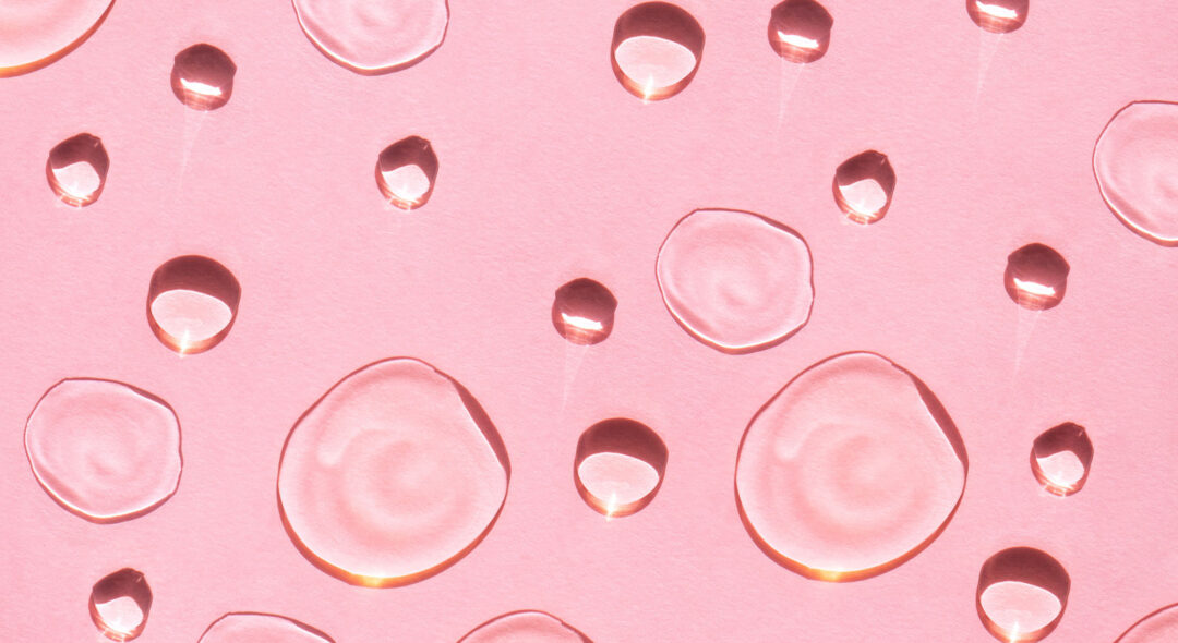 Drops of facial serum or essential oil on pink background