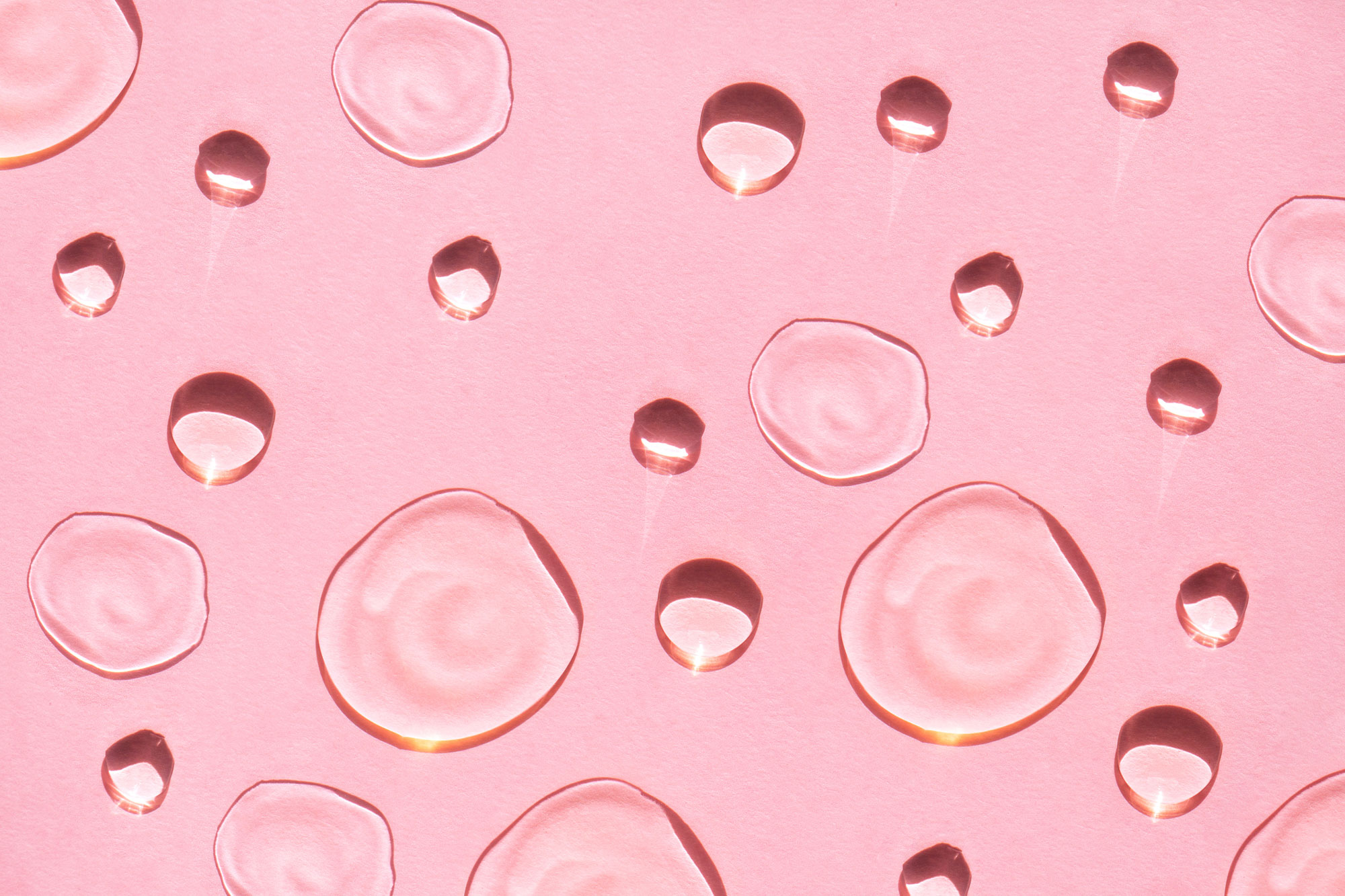 Drops of facial serum or essential oil on pink background