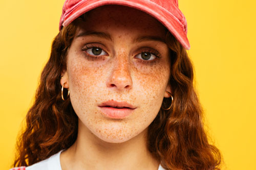 teen girl with freckles looking at camera in front of yellow background