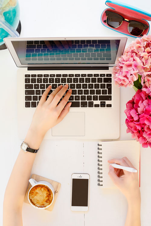 overhead shot of hand taking notes and using laptop in office