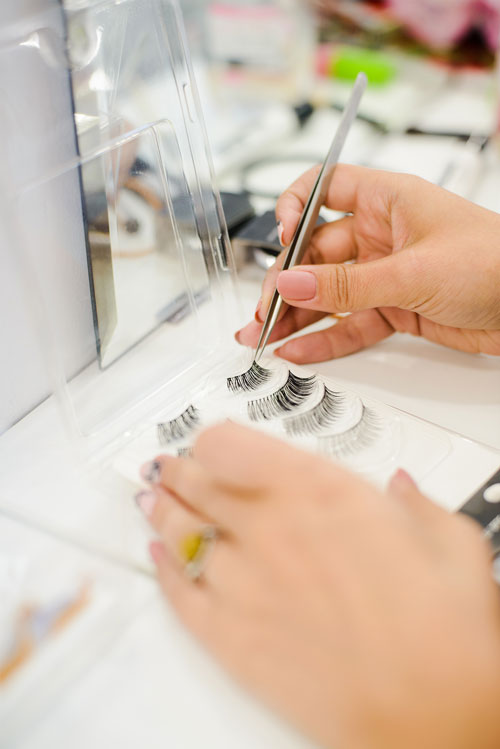 womans hand with tweezer takes artificial false eyelashes, view from angle above
