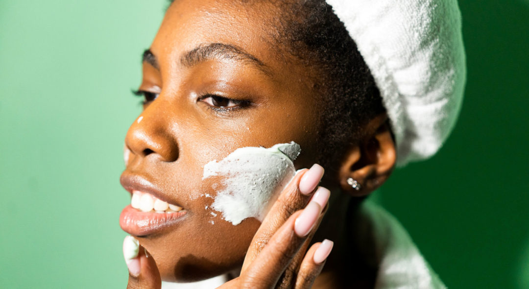 Close-up of woman applying cream on face while standing against green background