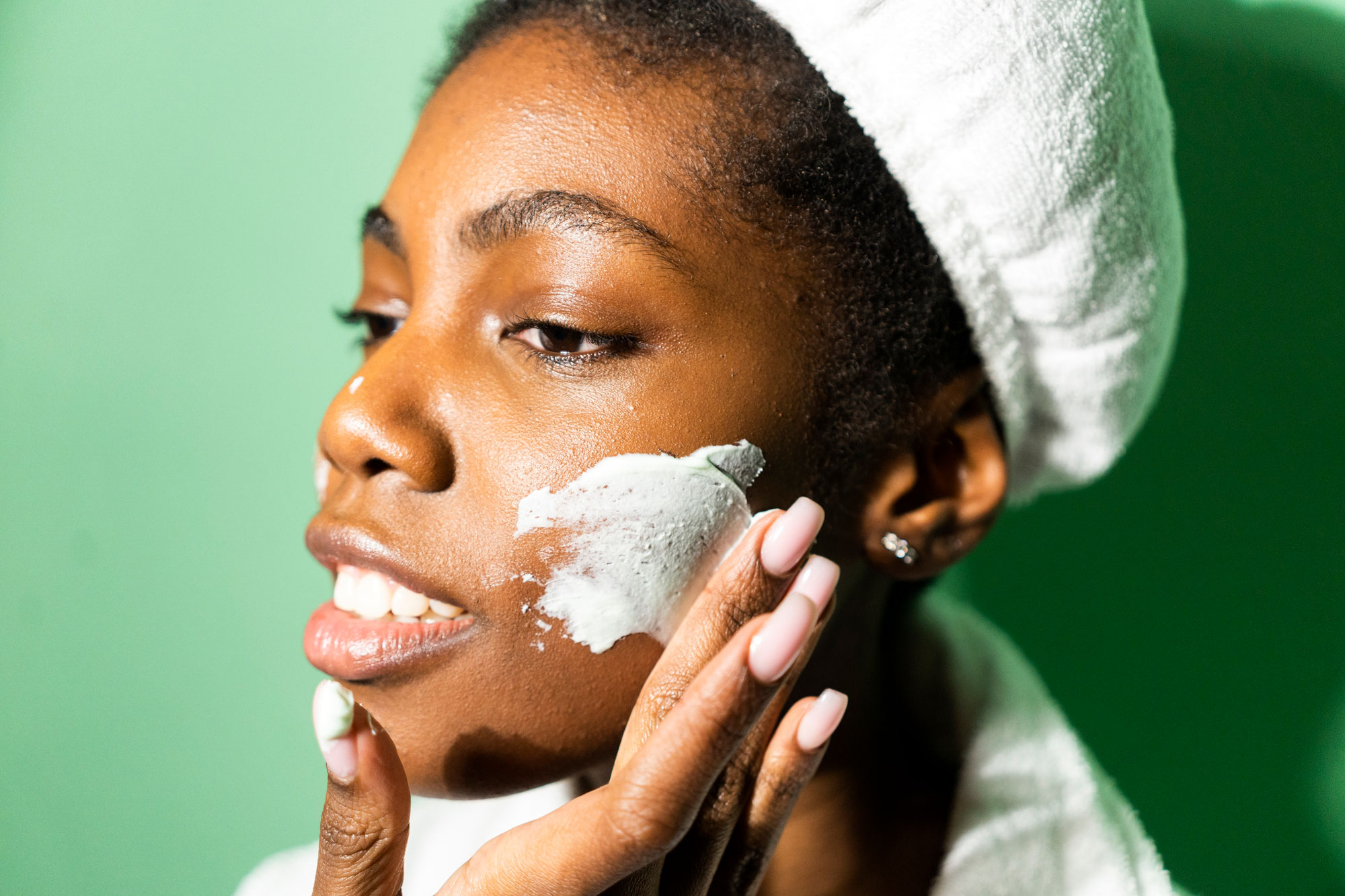 Close-up of woman applying cream on face while standing against green background