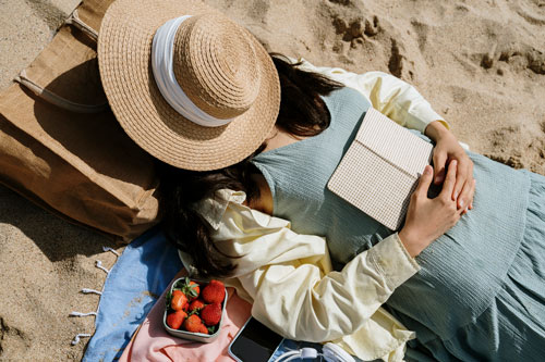 Woman covering face with hat while lying on beach - 