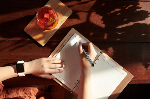 woman drinking fruit cocktail and writing in journal