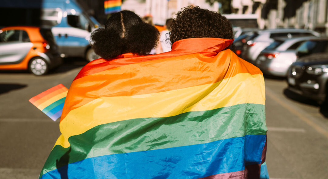 friends wrapped in rainbow flag on sunny day