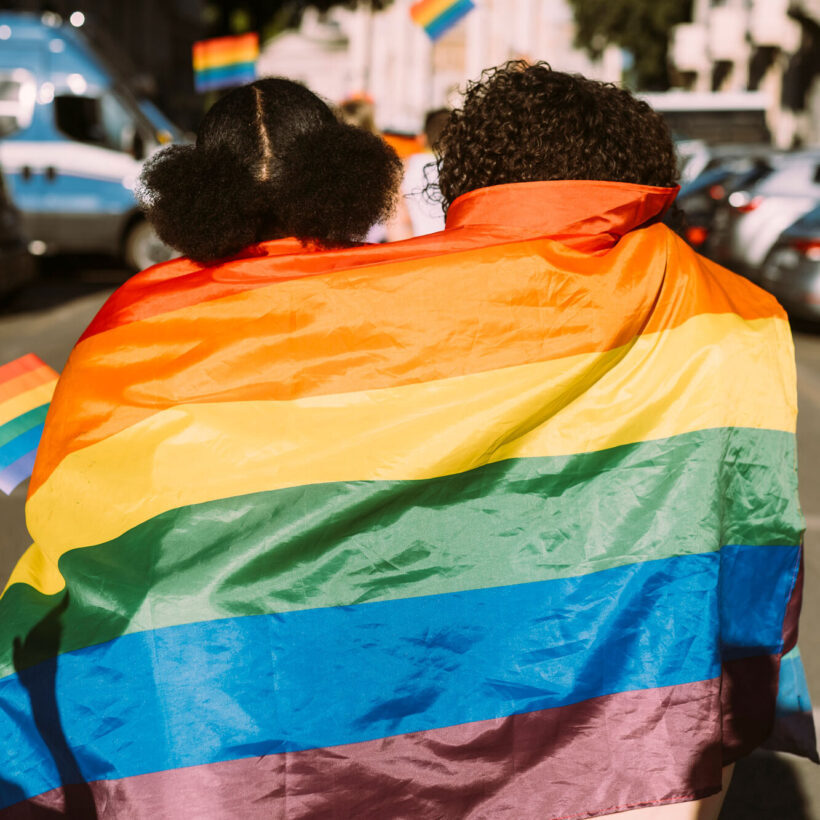 friends wrapped in rainbow flag on sunny day