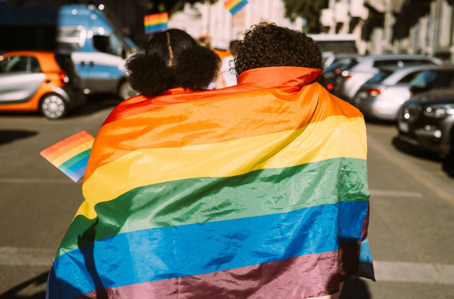 friends wrapped in rainbow flag on sunny day