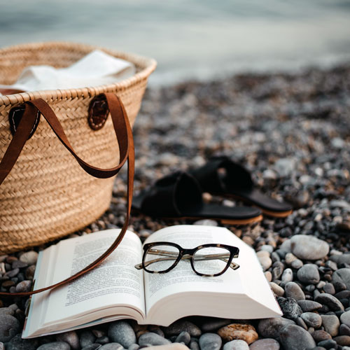 Close-Up Of Sunglasses Book And Basket On Pebbles At Beach