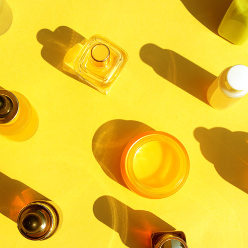 Facial Serum, Natural Essential Oil, Hand cream, Lip balm and Perfume in cosmetic bottles with dropper and bright sunny shadow on yellow color background.