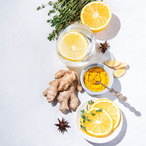 Flat lay with ingredients from turmeric, thyme, lemon, star anise and glass water with lemon on white background with hard shadows