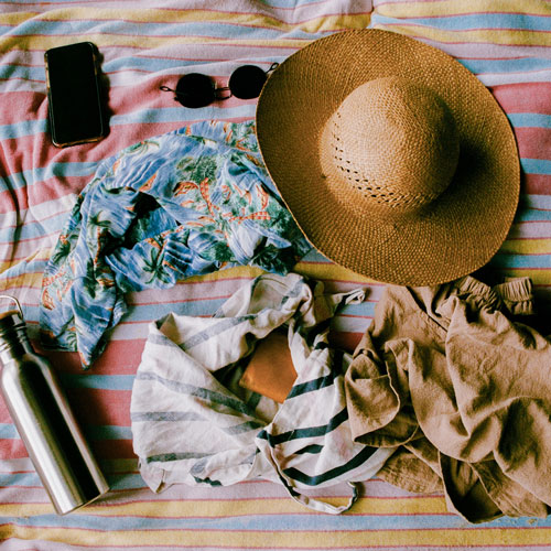 water bottle, sun hat, sunglasses and beach cover ups on towel in beach